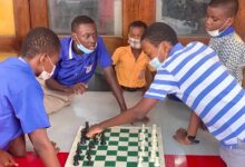 Selikem (hand stretched) playing chess whilst some students look on