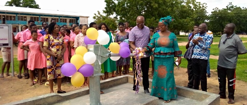 • Ms Babachuwey assisting a representative from the Ministries to cut a ribbon to officially inaugurate the borehole, looking on are students and staff of the school