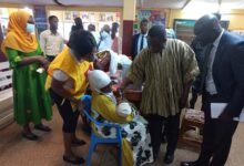Mr Kwasi Adu Gyan (middle) giving a drop of vaccine to a child, while Dr Adomako-Boateng looks on
