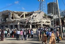Civilians gather near the ruins of a building at the scene of an explosion along K5 Street in Mogadishu, Somalia