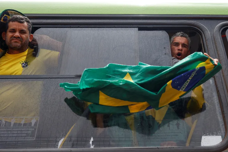 • A man holds a Brazilian flag outside the window of a bus