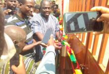 Dr Joshua Makubu (in smock) being assisted by other officials to cut the tape to inaugurate the classroom block