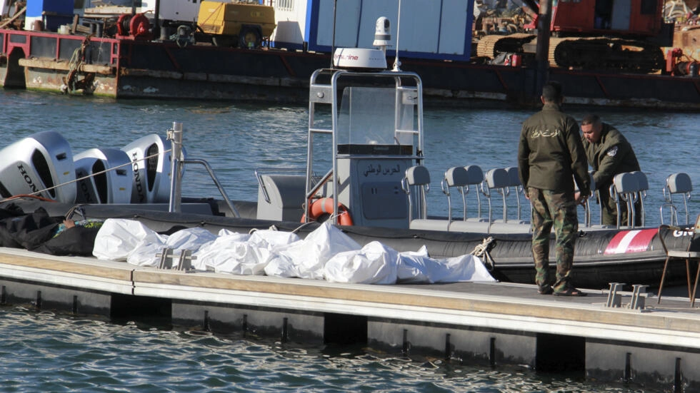 Tunisian coast guards stand next to the covered dead bodies of migrants in the port of Sfax